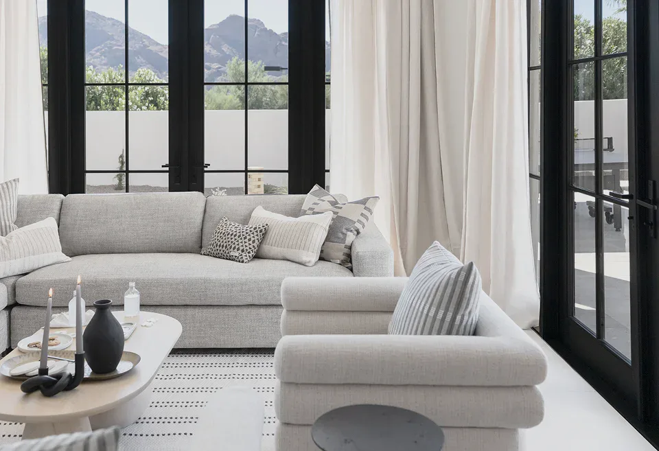 Luxury living room with large black-framed windows, neutral furnishings, and mountain views, featuring a custom sofa and elegant modern interior design