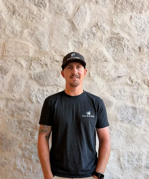 Portrait of Cody, E&S Builders team member wearing a cap, standing against a stone wall