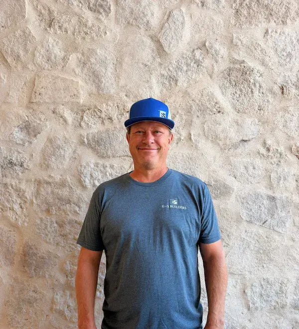 Portrait of Eric, E&S Builders team member wearing a blue cap, standing against a stone wall