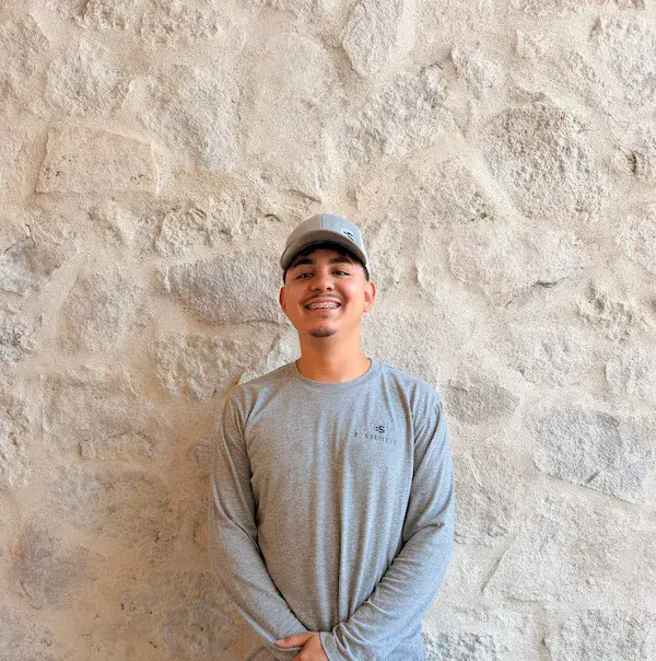 Portrait of Kelvin, E&S Builders team member wearing a cap, standing against a stone wall