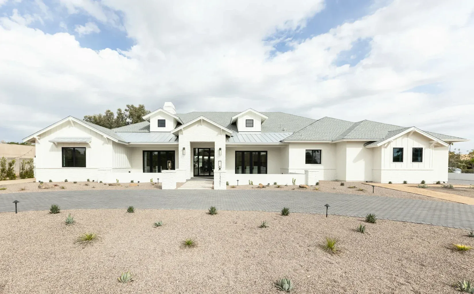 Modern white farmhouse with desert landscaping and gray roof