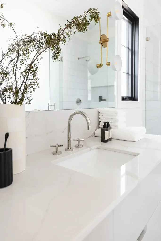 Modern white marble bathroom vanity with gold sconce and greenery