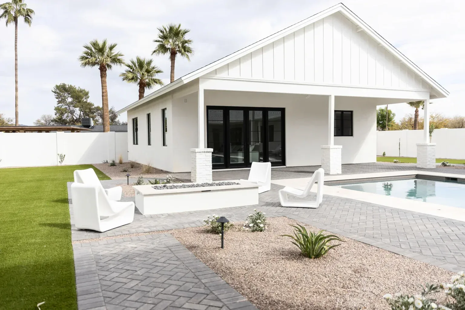 Modern white home backyard with pool, fire pit, and palm trees