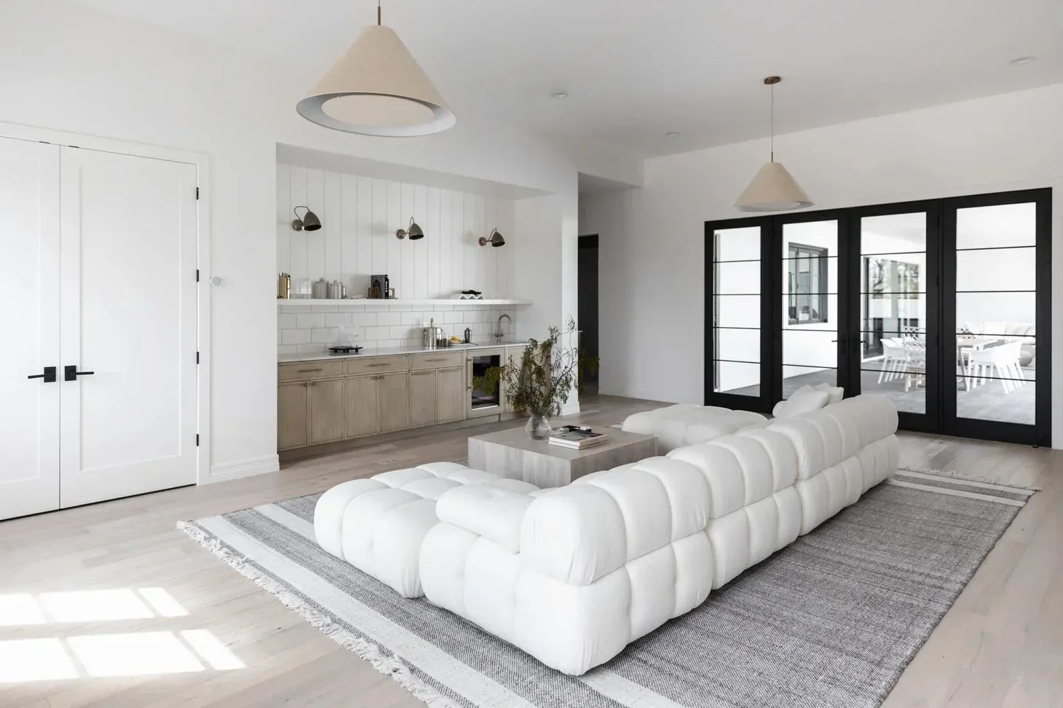Modern white living room with tufted sectional sofa and kitchenette
