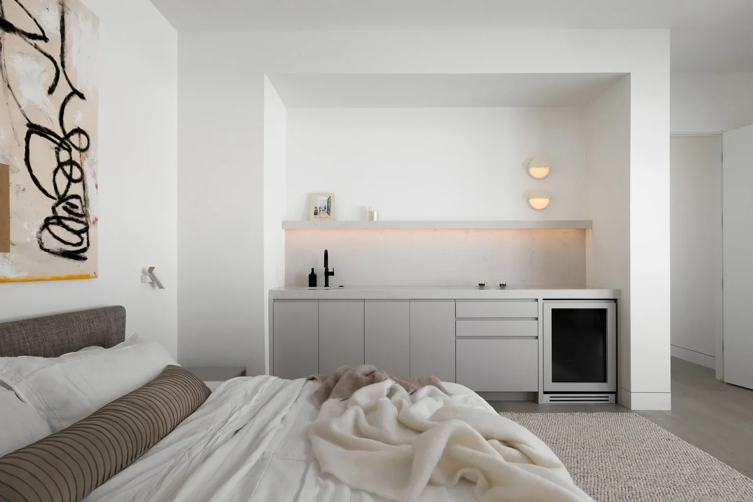 Modern minimalist bedroom with built-in kitchenette and abstract wall art