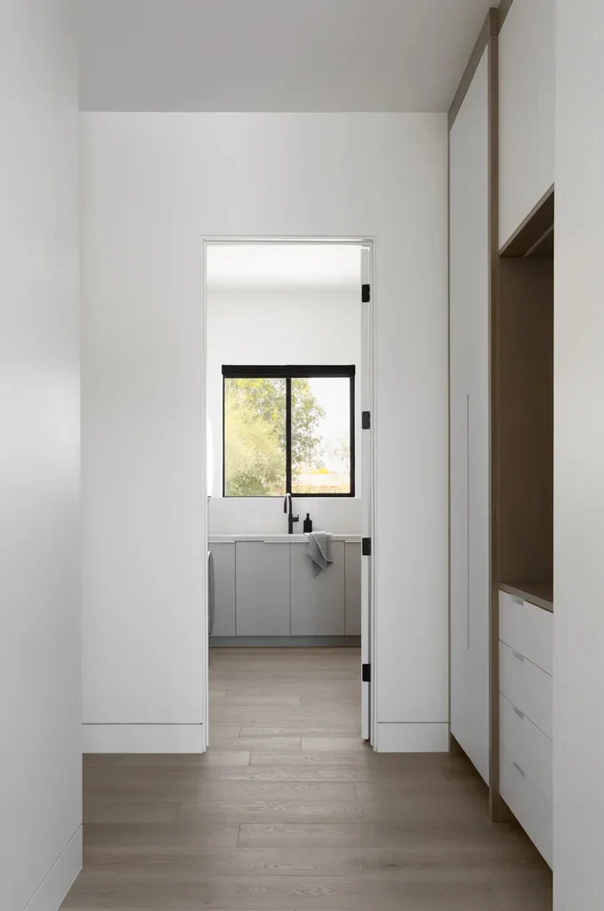 Modern hallway leading to minimalist white laundry room with window
