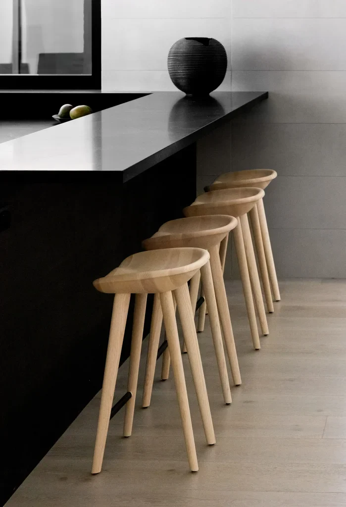 Four wooden bar stools lined up at black kitchen counter