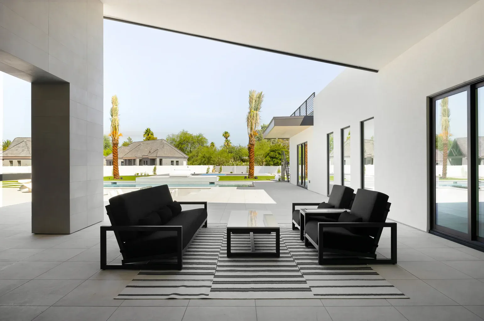 Modern covered patio with black furniture overlooking pool and palm trees