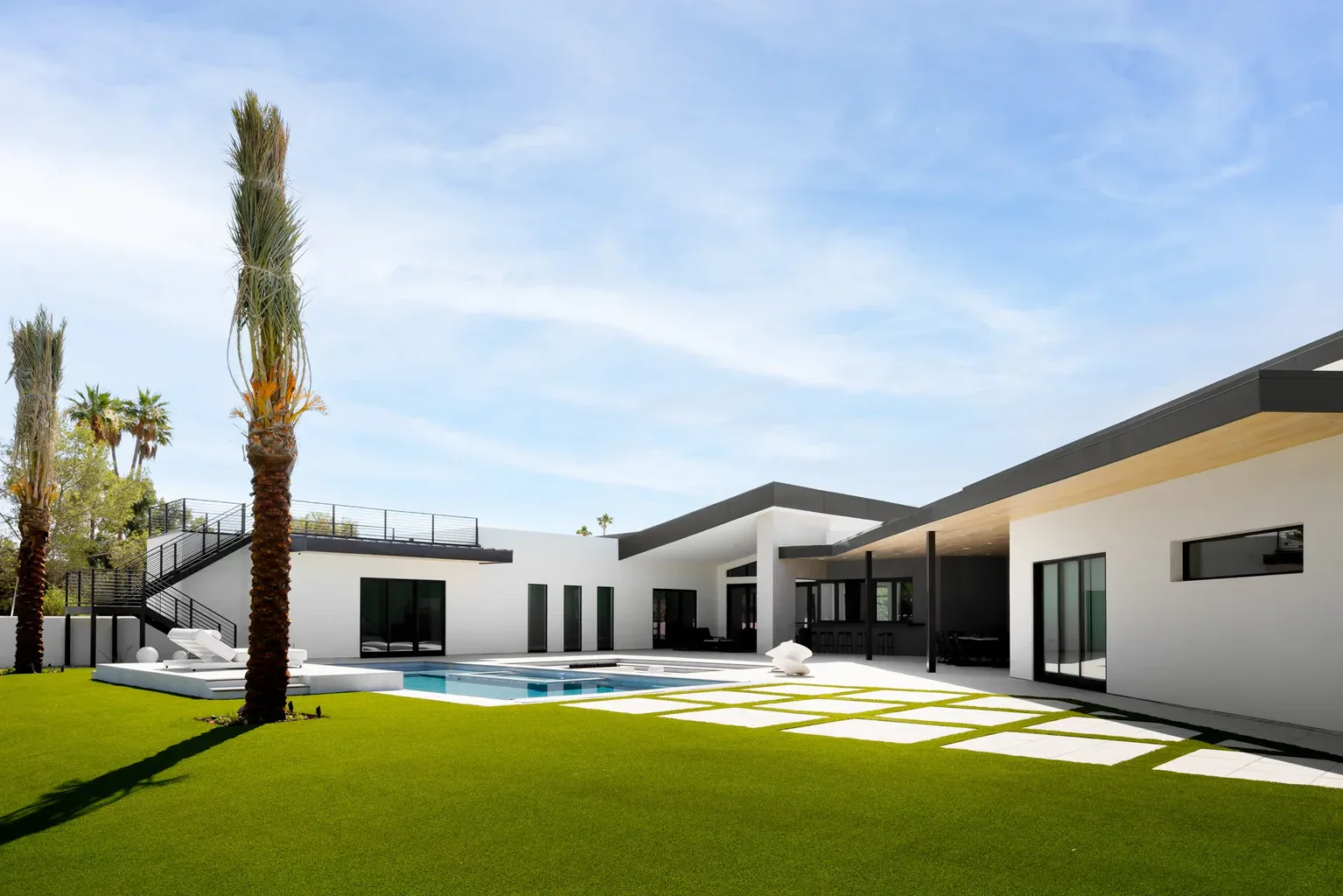Modern luxury home with pool, green lawn, and palm trees
