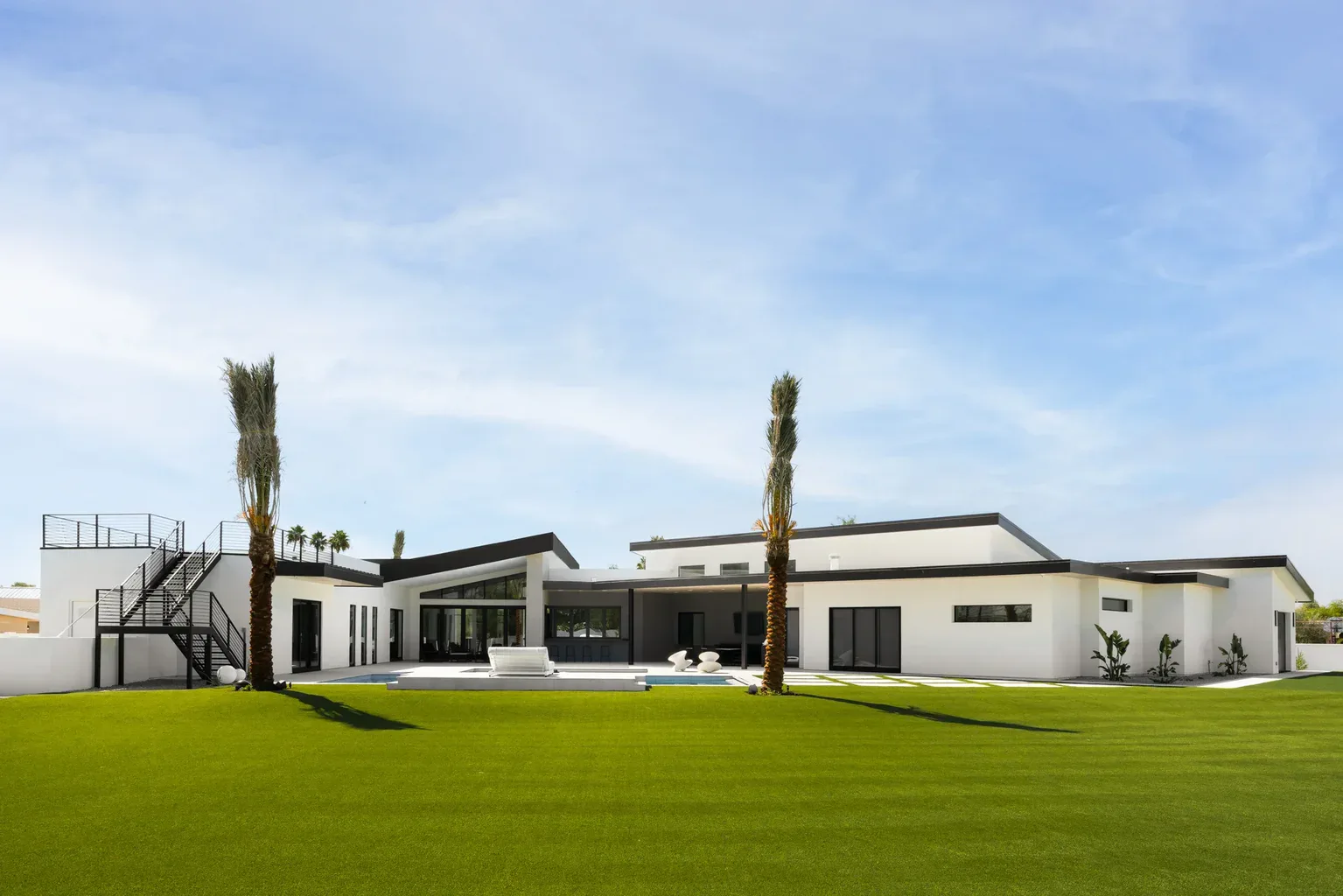 Modern white luxury home with palm trees and green lawn