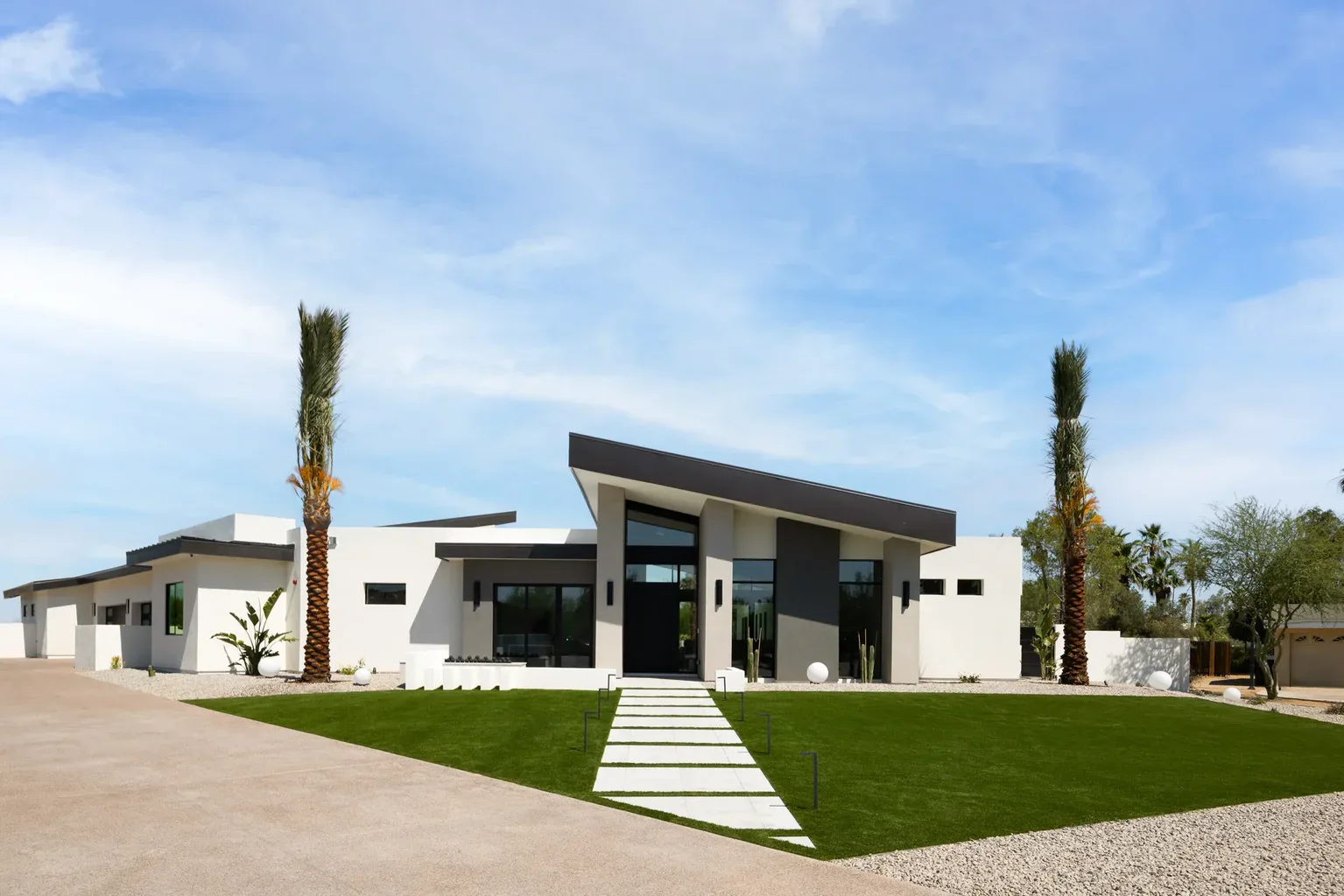 Modern white desert home with palm trees and green lawn