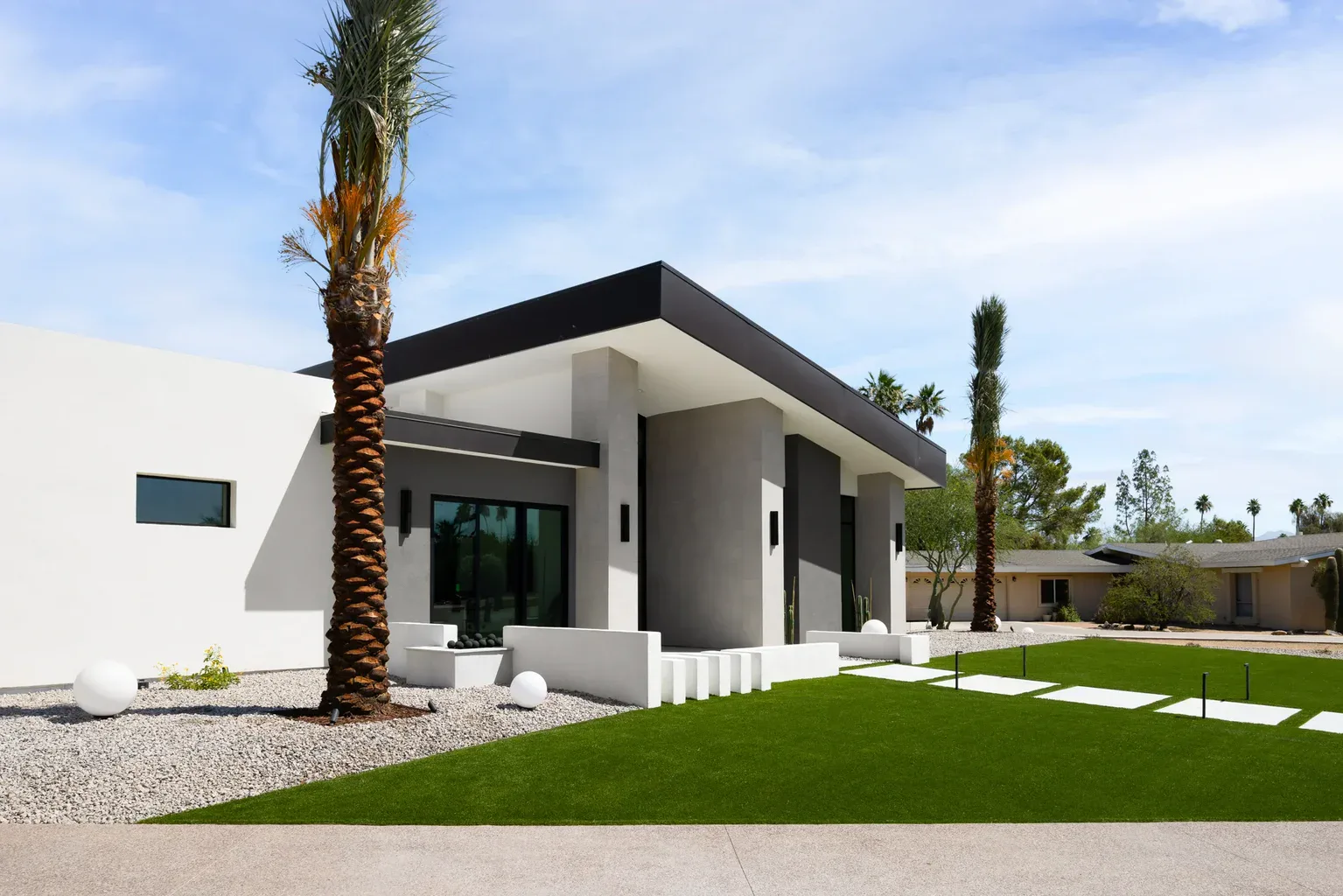 Modern desert home with flat roof, palm trees, and green lawn
