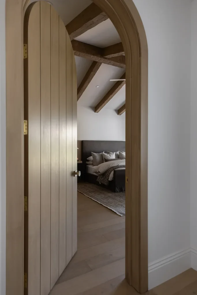 Arched wooden door opening to bedroom with exposed ceiling beams