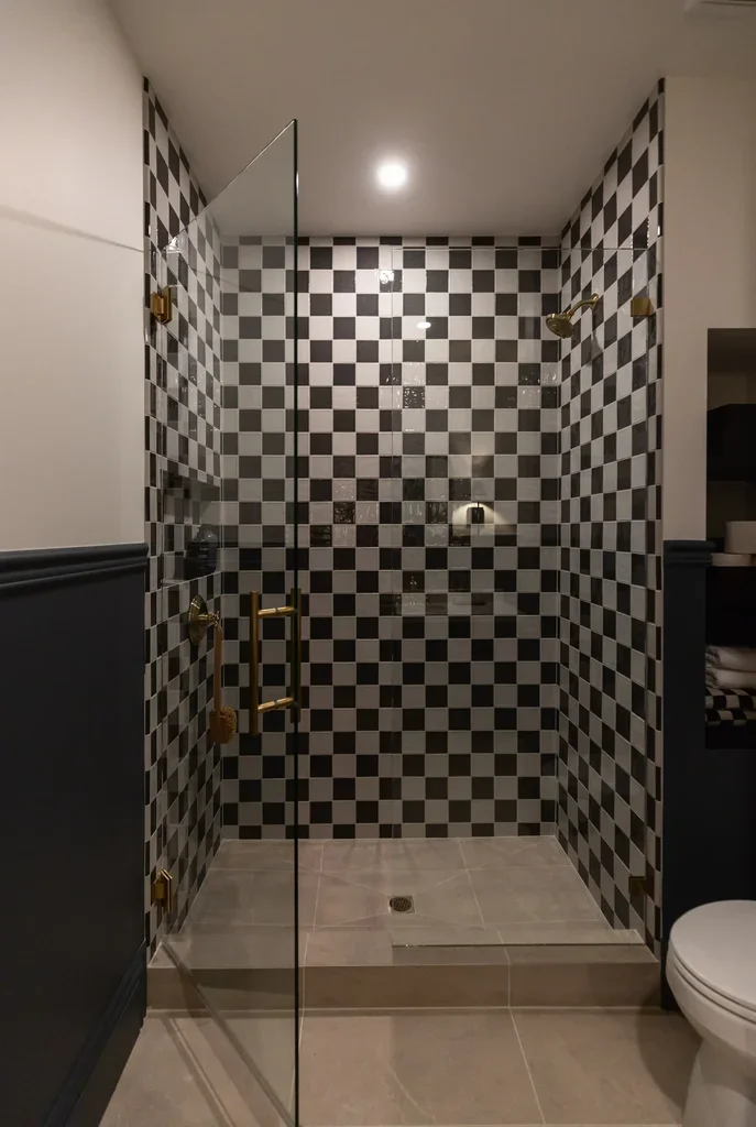 Glass shower with black and white checkered tiles and gold hardware