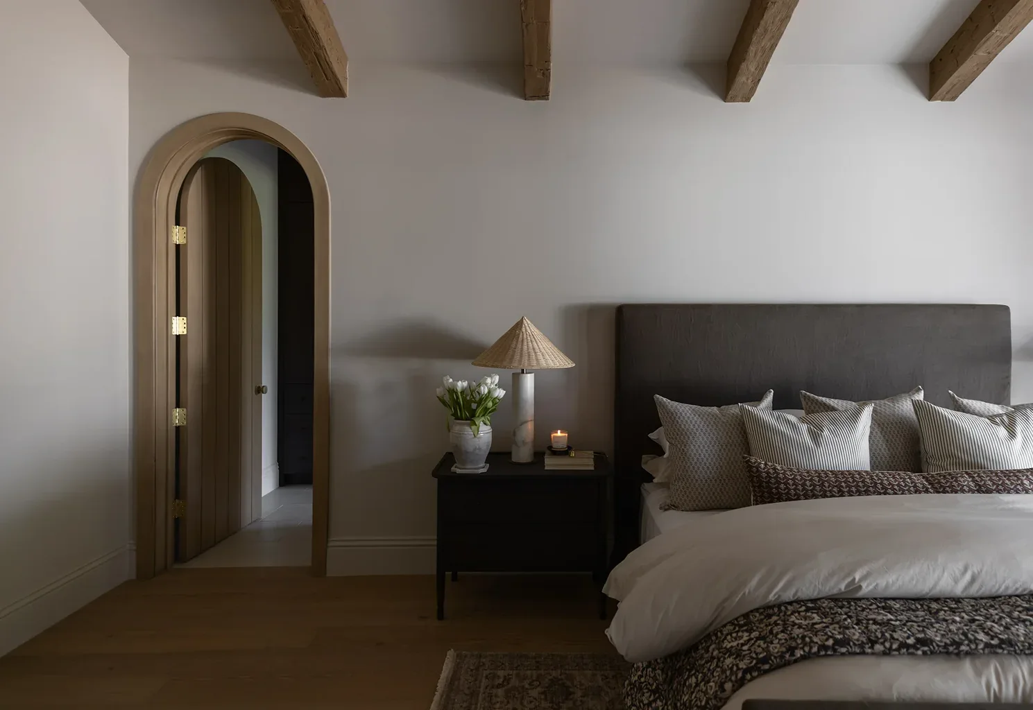 Elegant bedroom with arched doorway, exposed beams, and neutral decor