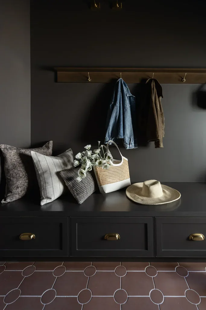 Dark mudroom bench with hooks, pillows, hat, and woven bag