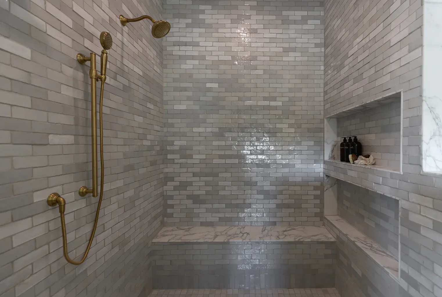 Luxury tiled shower with gold fixtures and marble bench seat